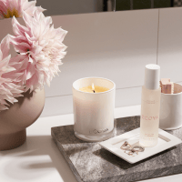 ECOYA candle on table with ECOYA room mist. Pink flowers in vase on table